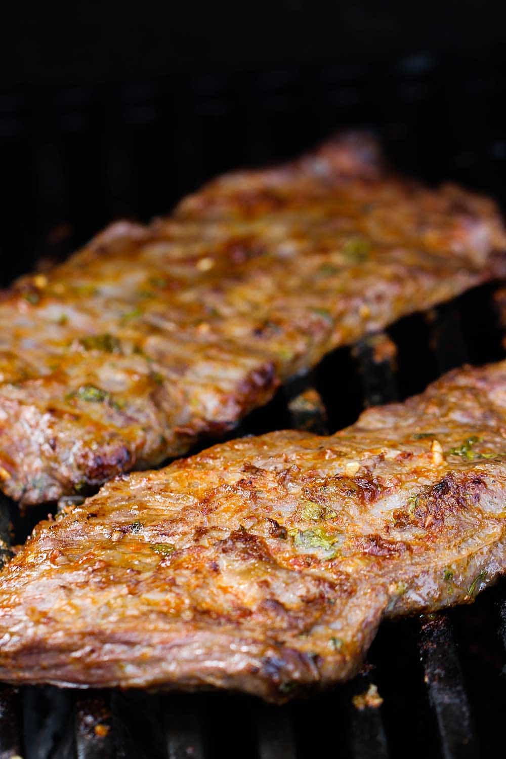 Two cuts of marinated skirt steak cooking on a gas grill for authentic steak fajitas. 