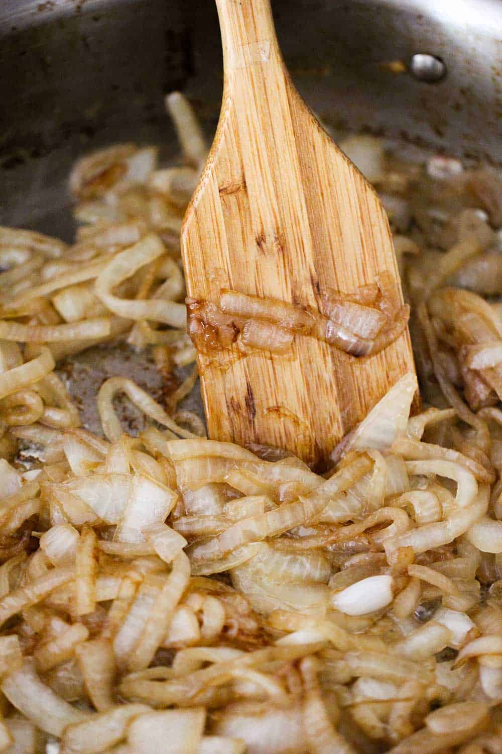 A large skillet with a wooden spoon stirring caramelized onions