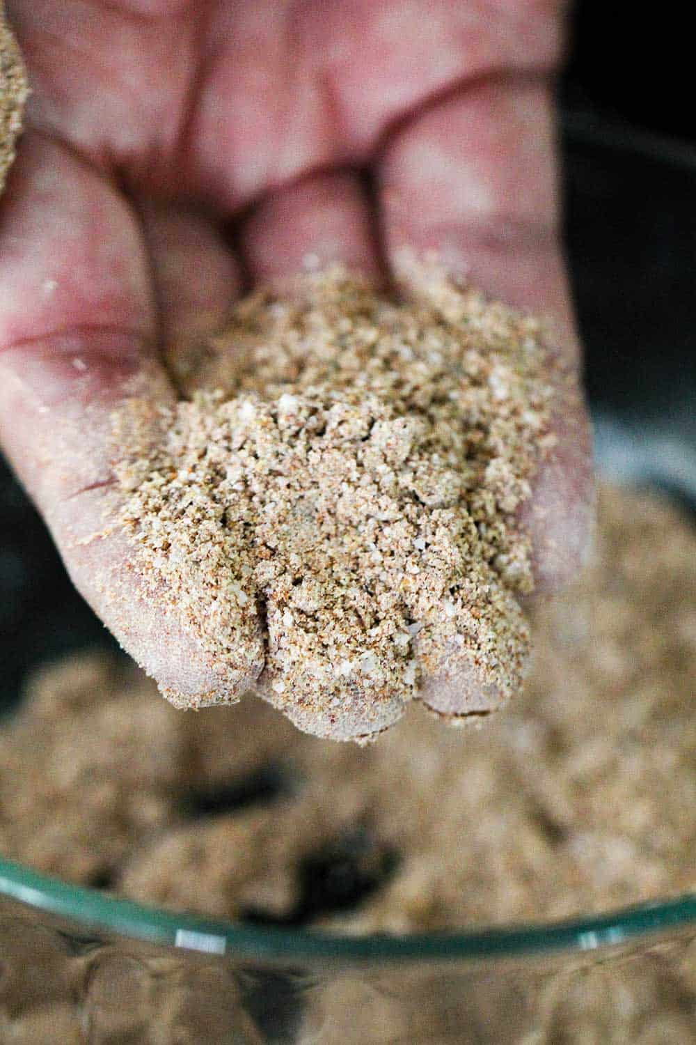 A hand holding a scoop of homemade fajita seasoning over a glass bowl. 