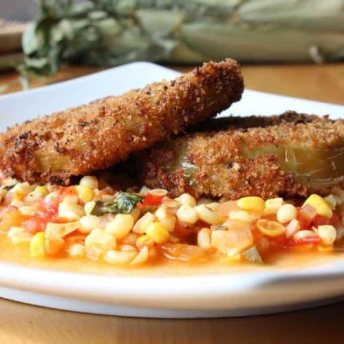 Fried green tomatoes on corn and tomato saute on a white plate