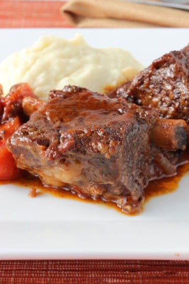 A white square plate of braised short ribs, carrots, and mashed potatoes.