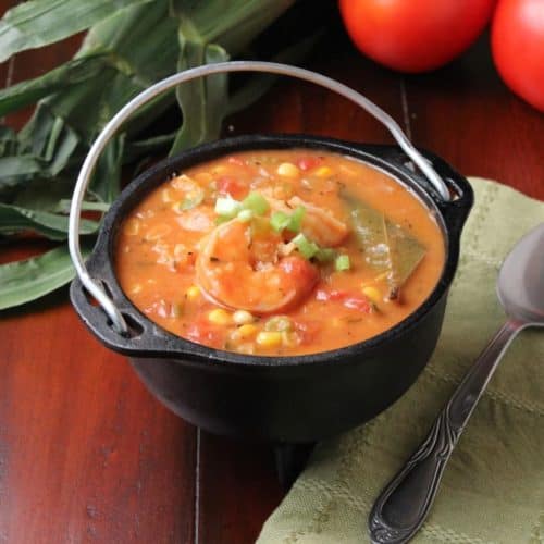 Shrimp, tomatoes, and corn stew next to a green napkin and spoon