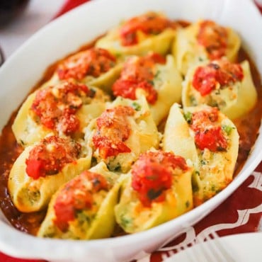 An oval white baking dish filled with cooked Italian stuffed shells all sitting on a layer of marinara sauce.