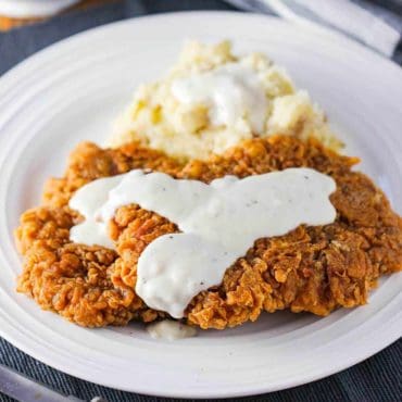 A plate of Southern chicken fried steak with mashed potatoes and cream gravy.