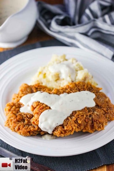 Chicken fried steak covered in cream gravy with mashed potatoes on the side.