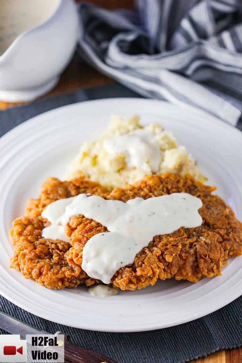 Chicken fried steak covered in cream gravy with mashed potatoes on the side. 