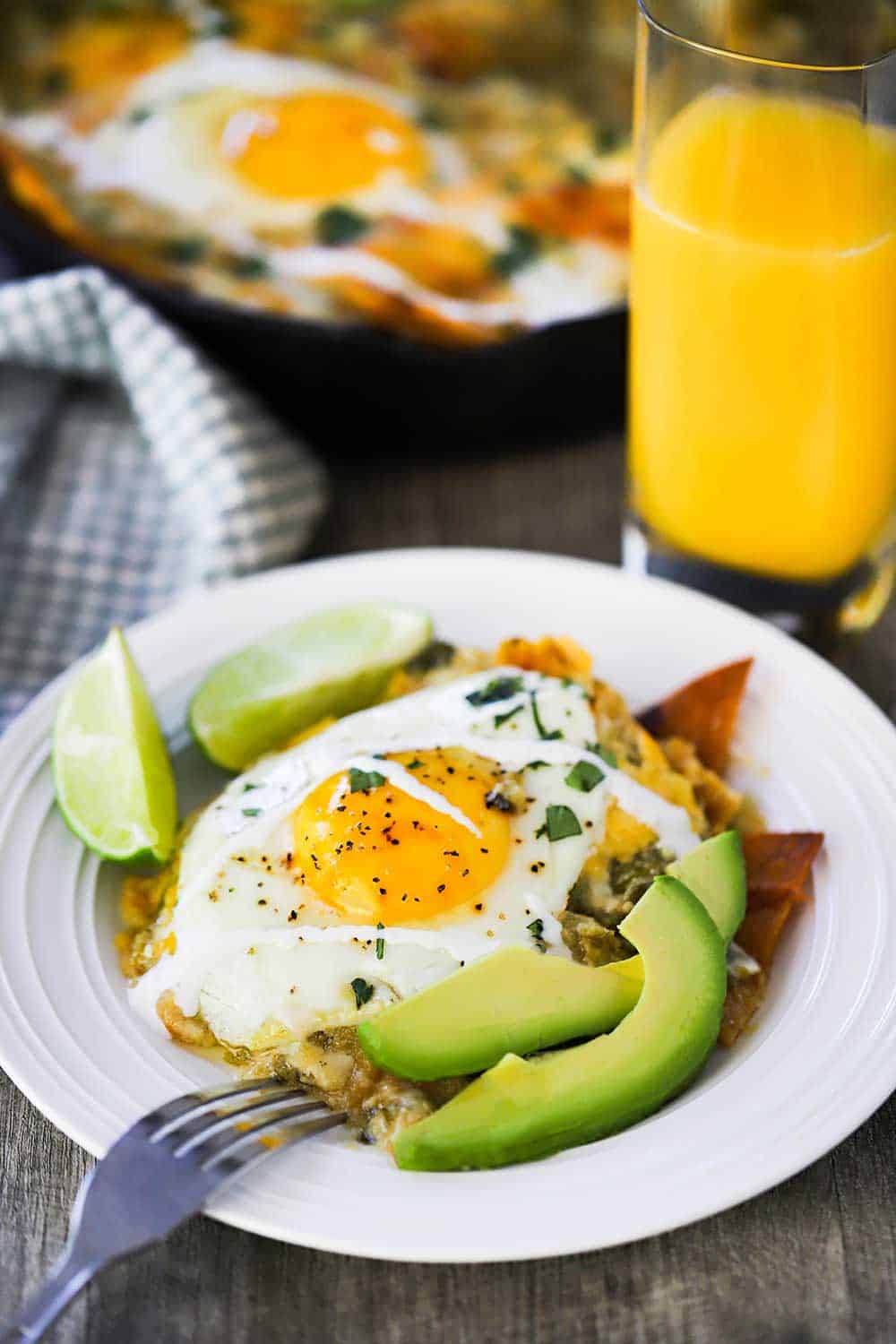 A white plate of chilaquiles topped with a fried egg next to a glass of orange juice. 