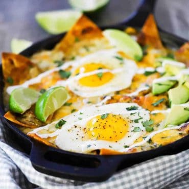 A close-up view of a cast-iron skillet filled with chilaquiles topped with two sunny side up fried eggs.