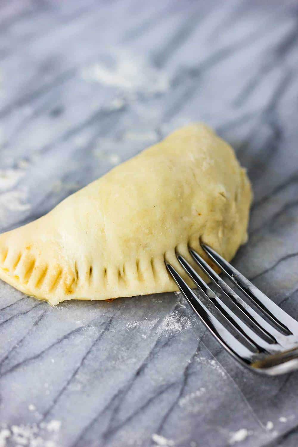 A fork crimping the edges of an uncooked classic meat pie
