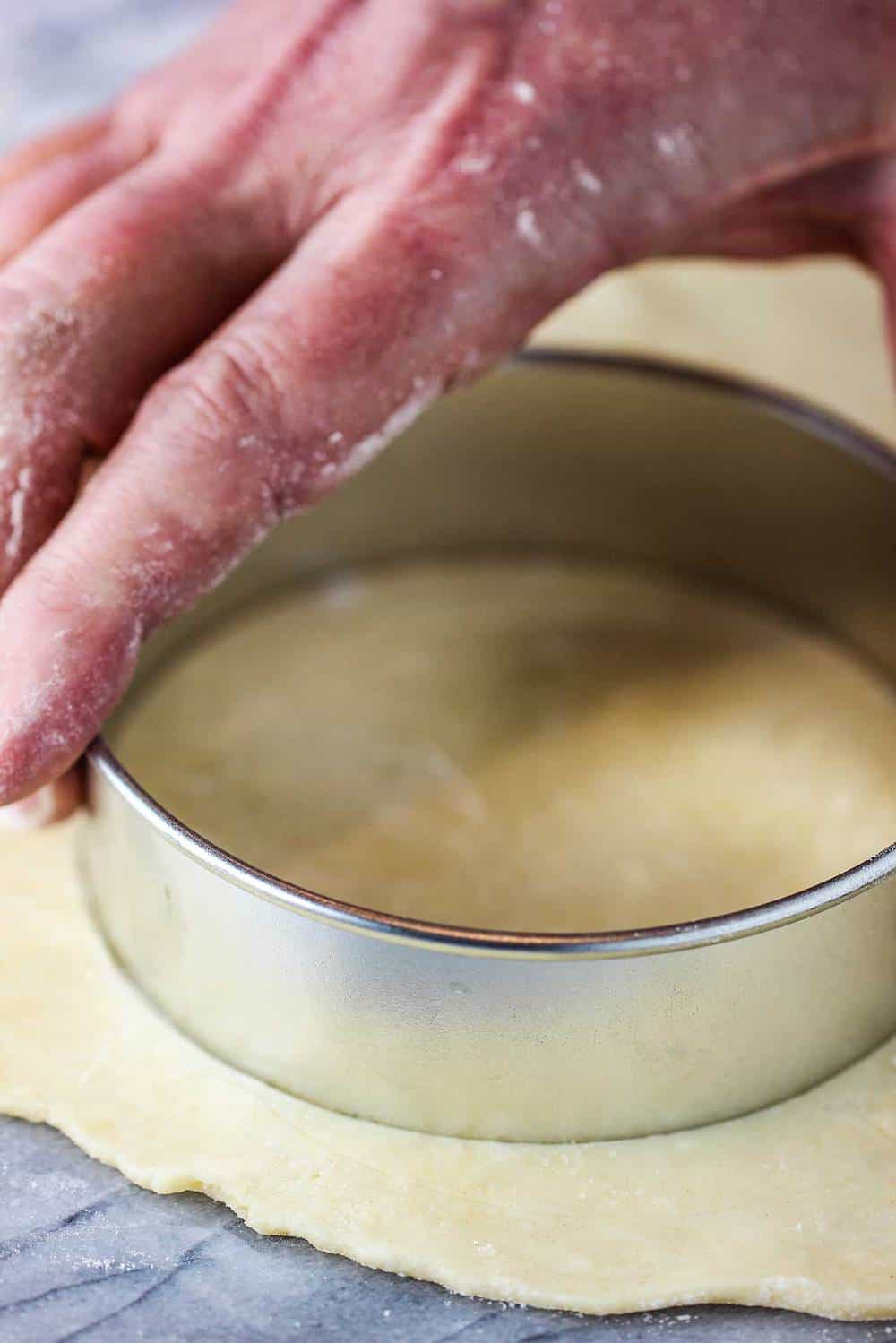 A hand using a dough cutter for the crust of classic meat pie