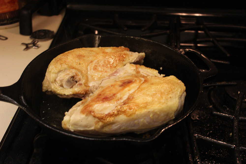 A skillet roasting chicken on a stove
