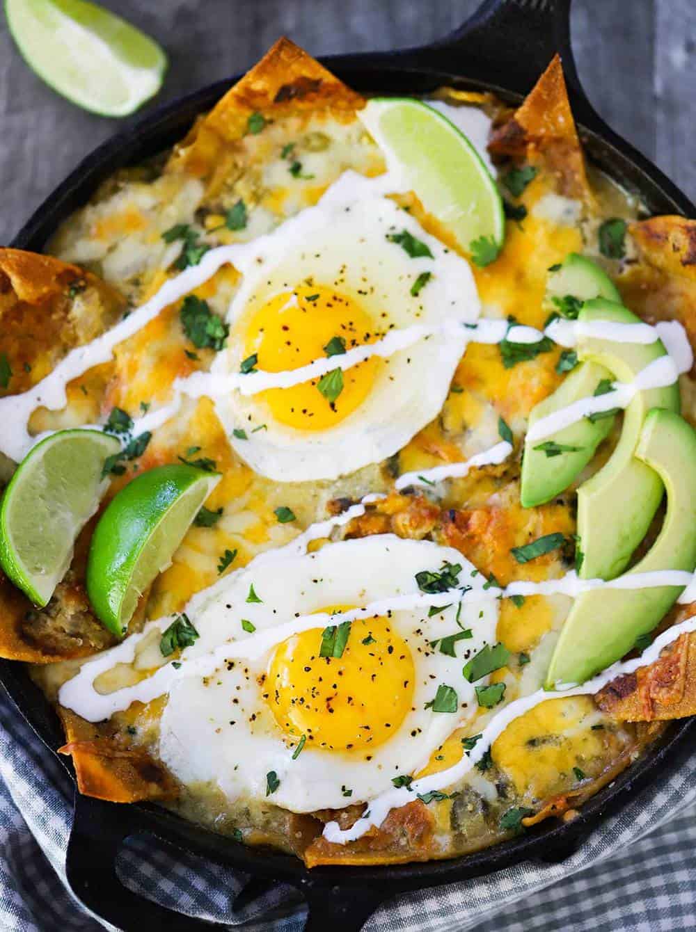 An overhead view of chilaquiles in a cast-iron skillet with 2 slices of lime and sliced avocado on top.