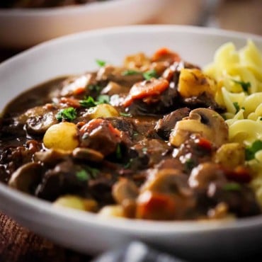 A white bowl filled with beef bourguignon and buttered egg noodles.