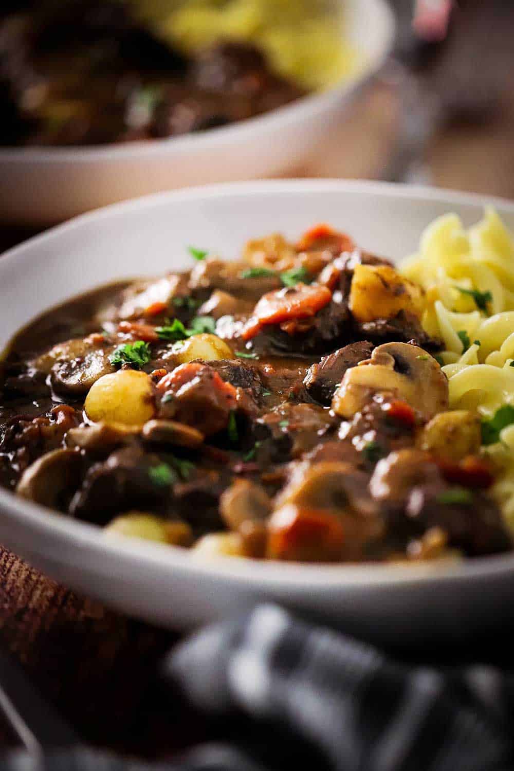 A white bowl filled with beef bourguignon and buttered egg noodles. 