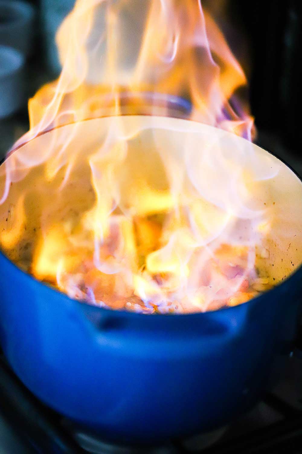 A large blue Dutch oven filled with flames after vegetables have been ignited from Cognac. 