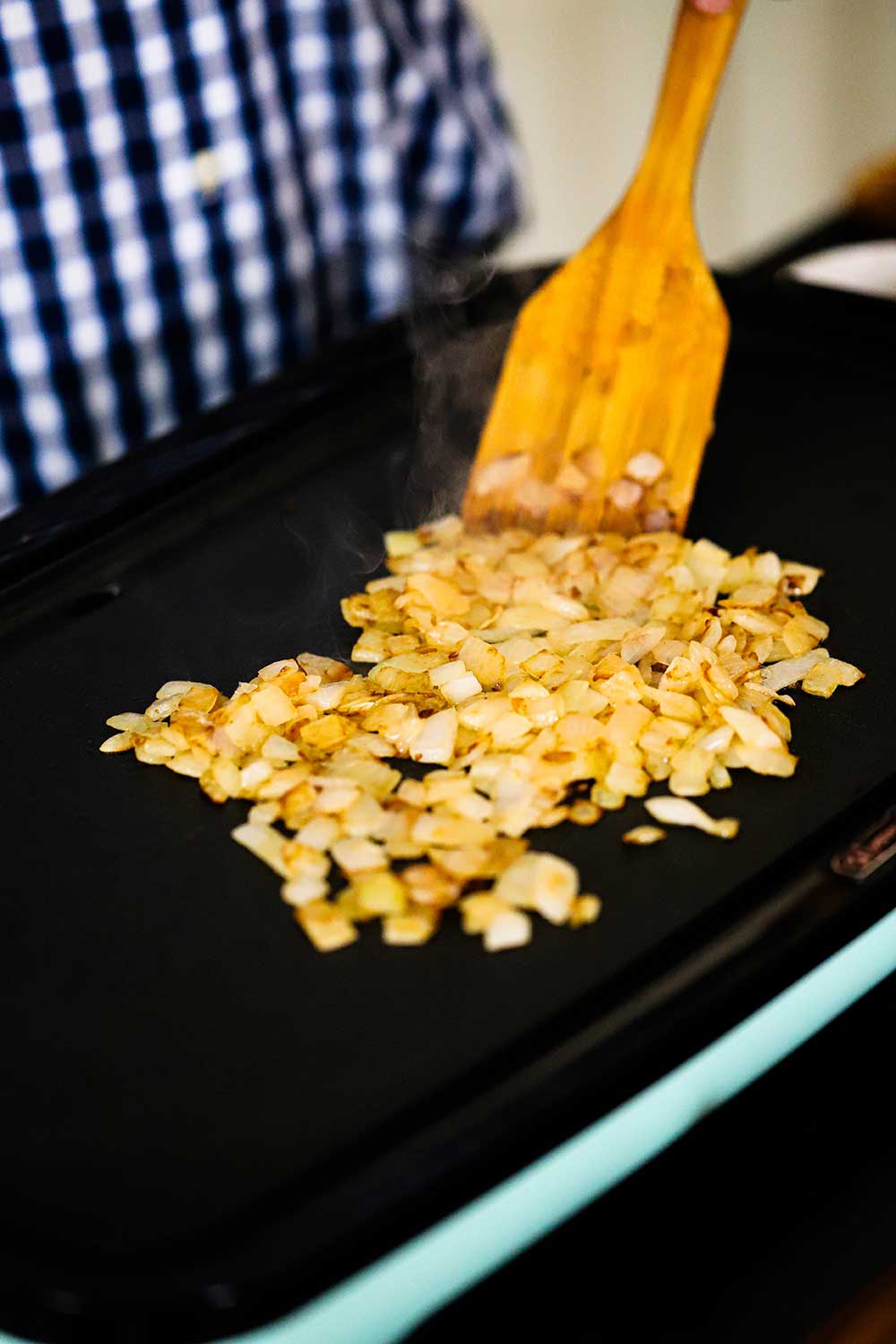 A person stirring chopped caramelized onions on a hot griddle. 