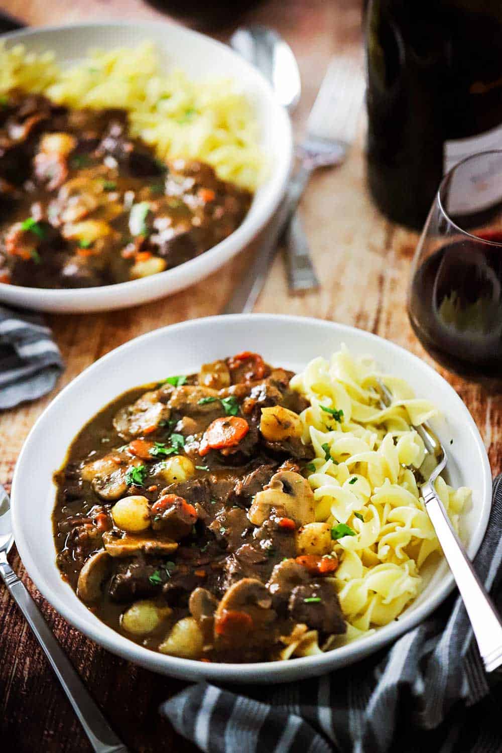 Two white bowls filled with beef bourguignon and buttered egg noodles. 