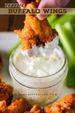 A hand plunging a classic buffalo wings into a jar of homemade blued cheese dressing.