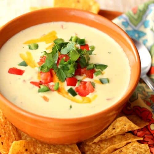 Jalapeño Cilantro Cheddar Soup in an orange bowl next to a patterned napkin and spoon