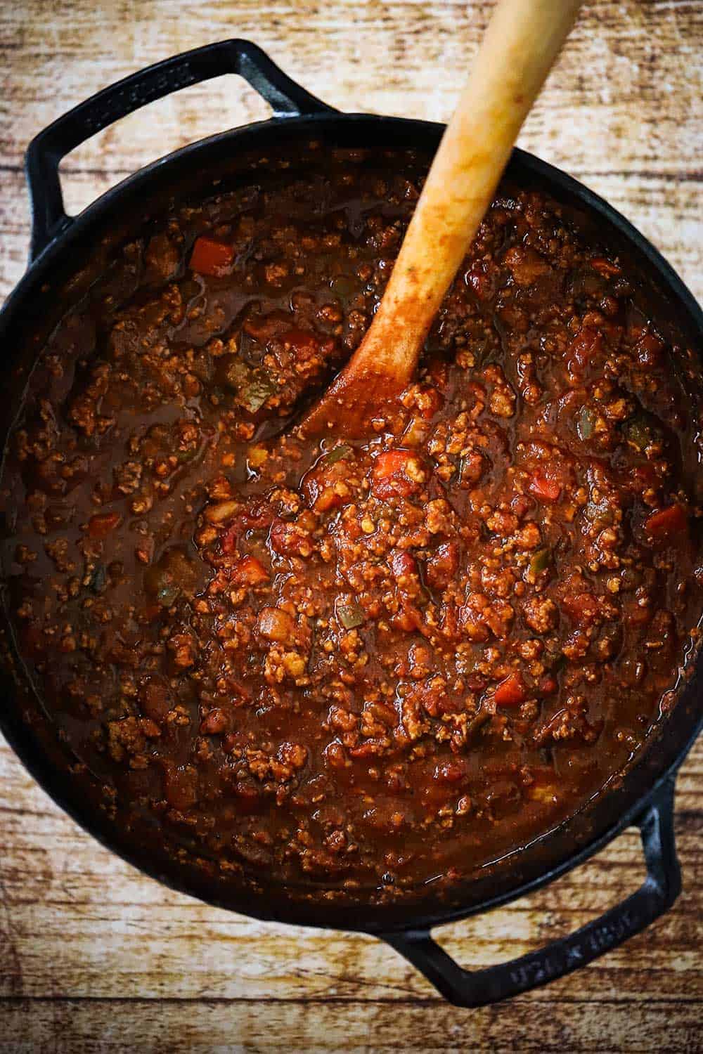 A large black cast-iron pot filled with turkey chili with a wooden spoon in the middle of it.