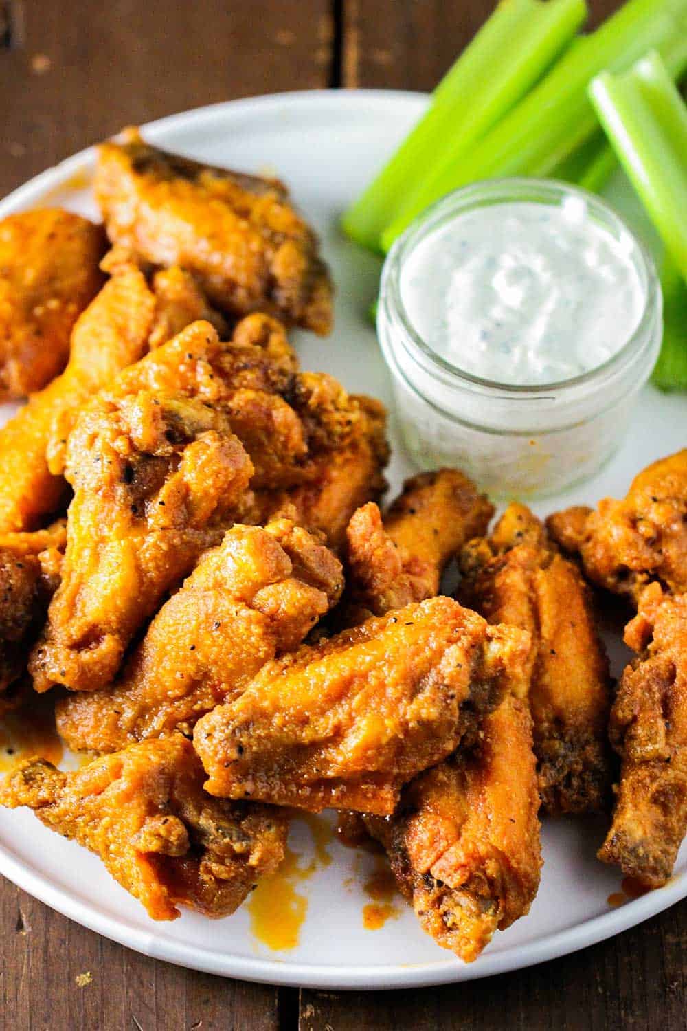 A round white platter of classic buffalo wings with a dish of blue cheese dressing and cut celery. 