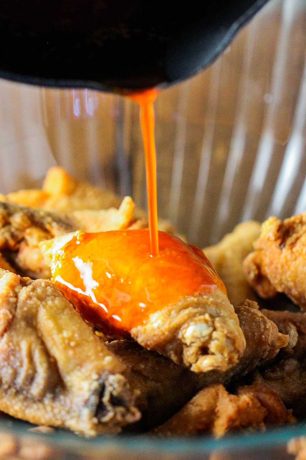 A pan pouring wing sauce over fried chicken wings. 