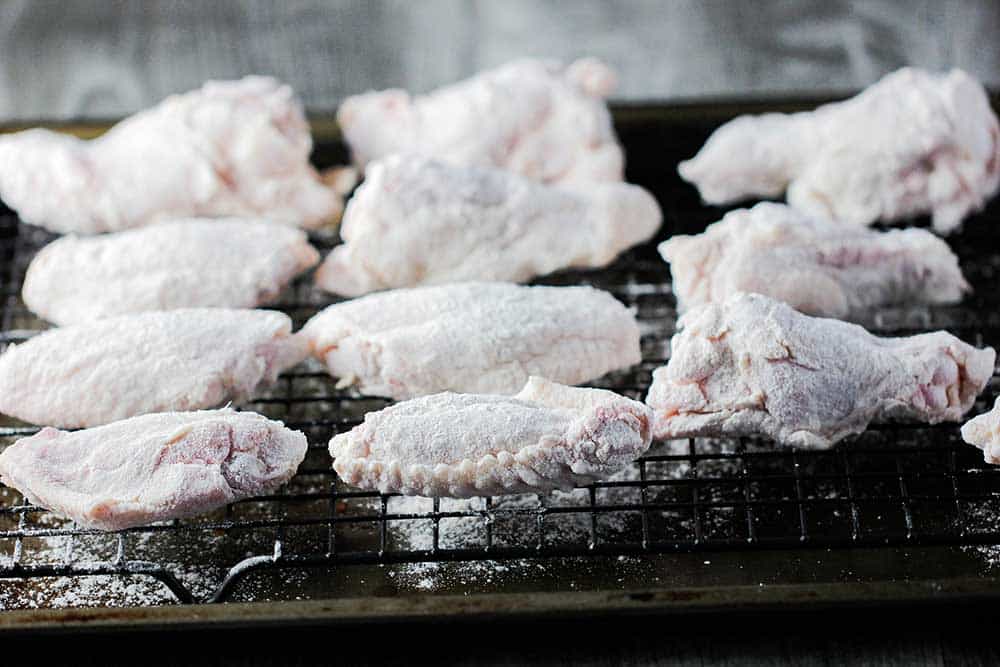 A baking rack filled with chicken wings that are coated with seasoned flour. 