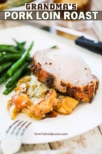 A white dinner plate filled with a slice of roasted pork loin and roasted apples and fennel and steamed green beans.