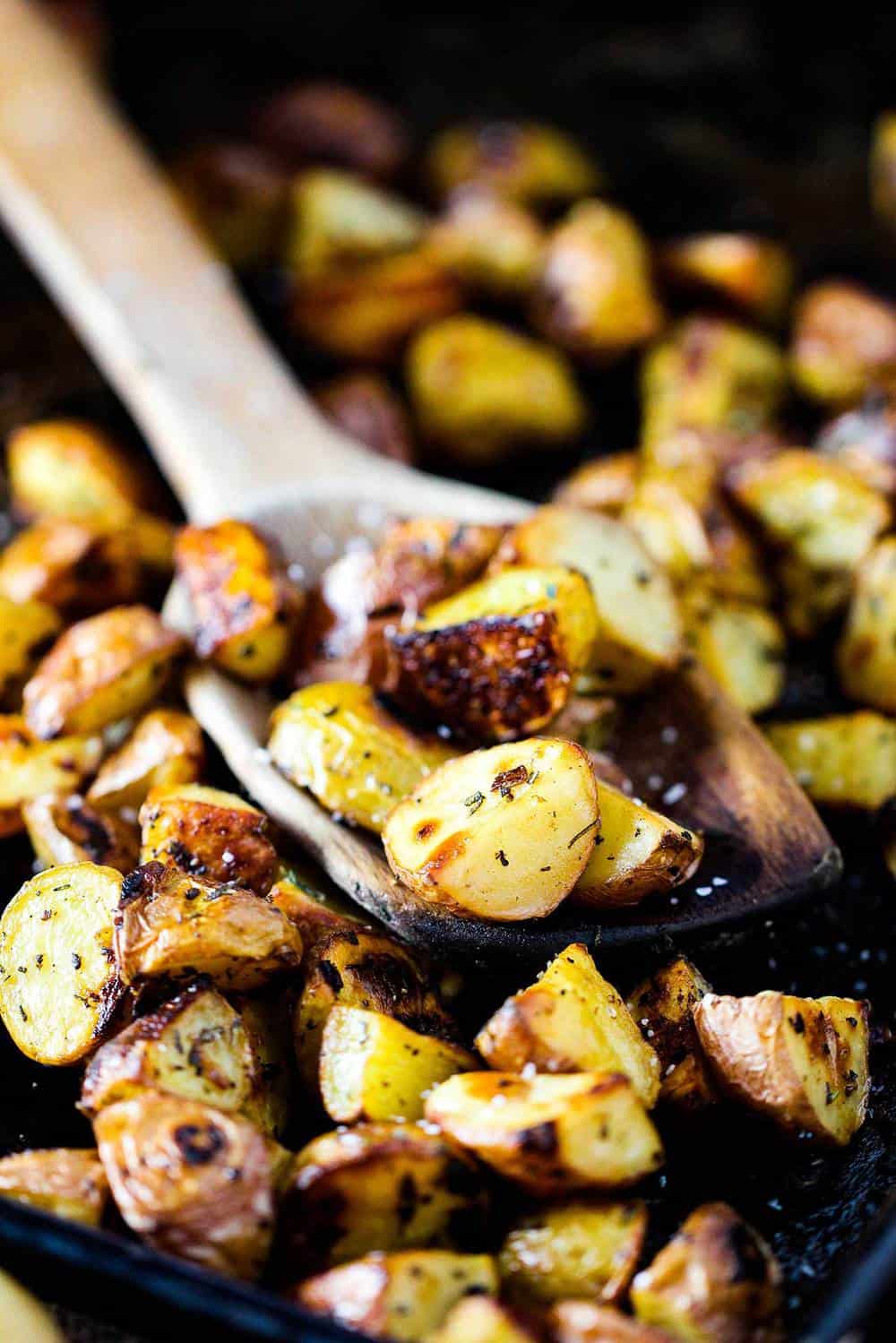 A wooden spoon scooping up roasted potatoes from a baking sheet.