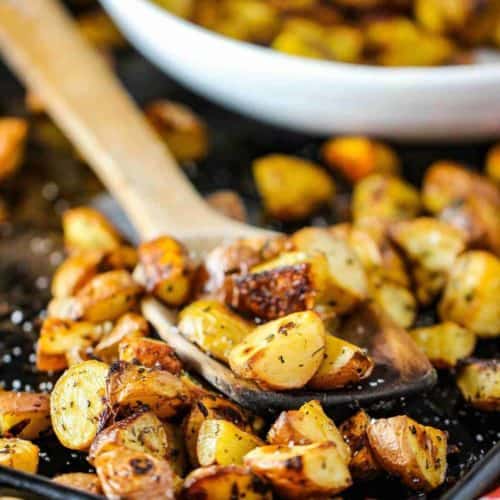 Roasted potatoes with balsamic and herbs on a baking sheet with a wooden spoon.