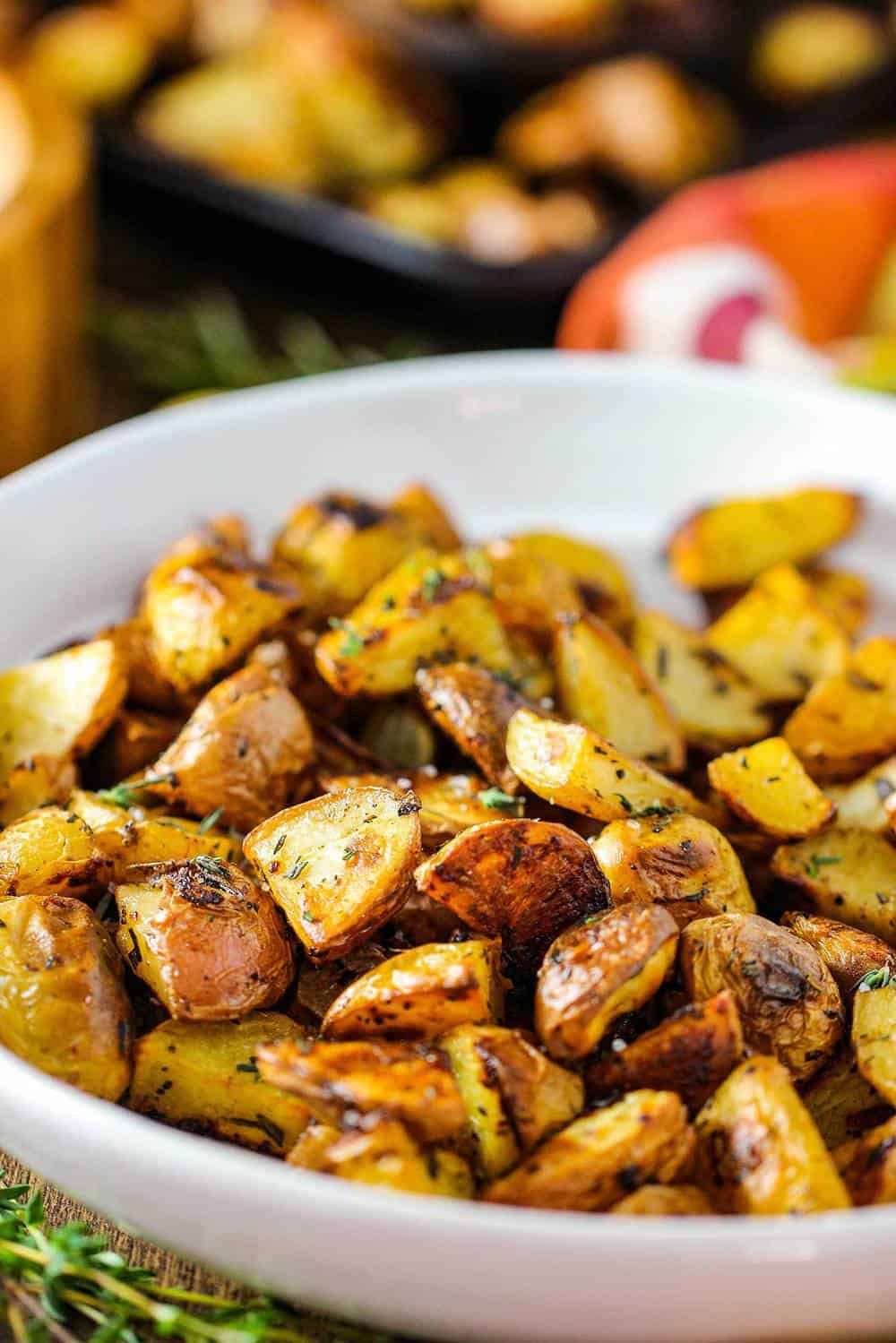 Roasted potatoes with balsamic and herbs in a white bowl. 