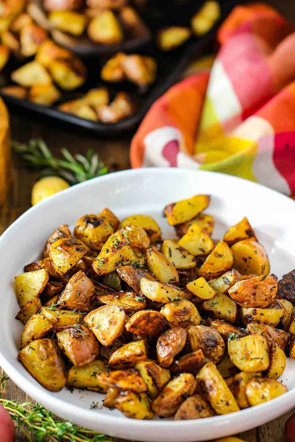 Roasted potatoes with balsamic and herbs in a white bowl with a colorful napkin next to it. 