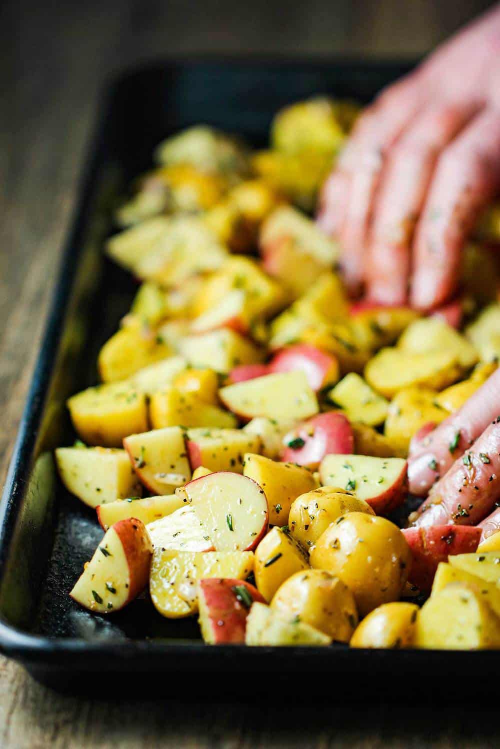 Cut baby potatoes being spread out on a baking sheet by two hands. 