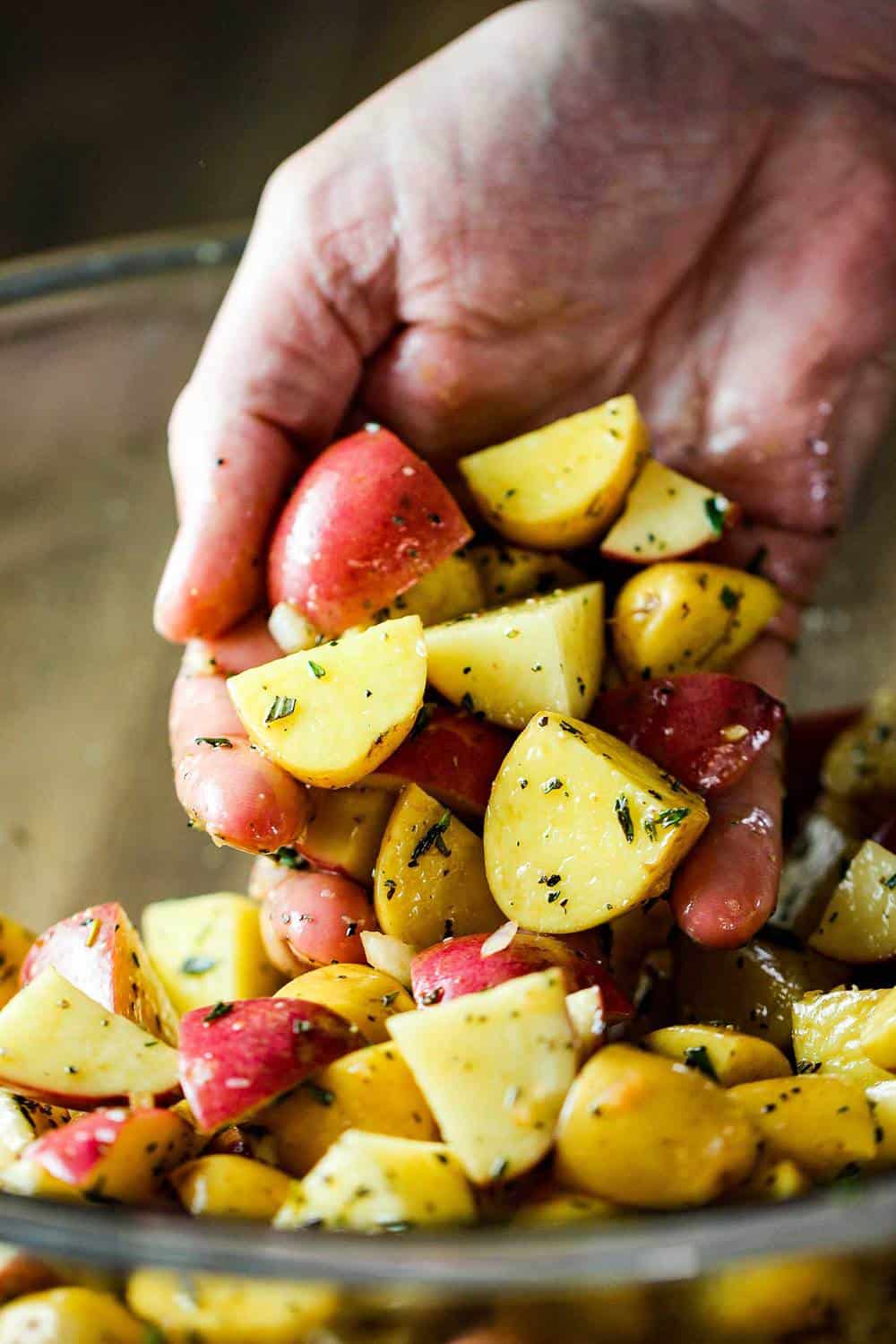 Baby potatoes with herbs and balsamic in a bowl and a hand tossing them. 