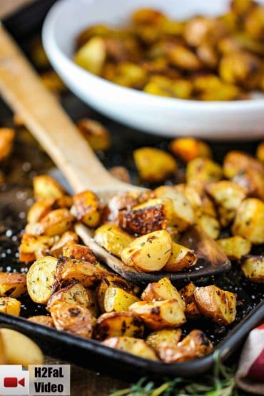 Roasted potatoes with balsamic and herbs on a baking sheet with a wooden spoon.
