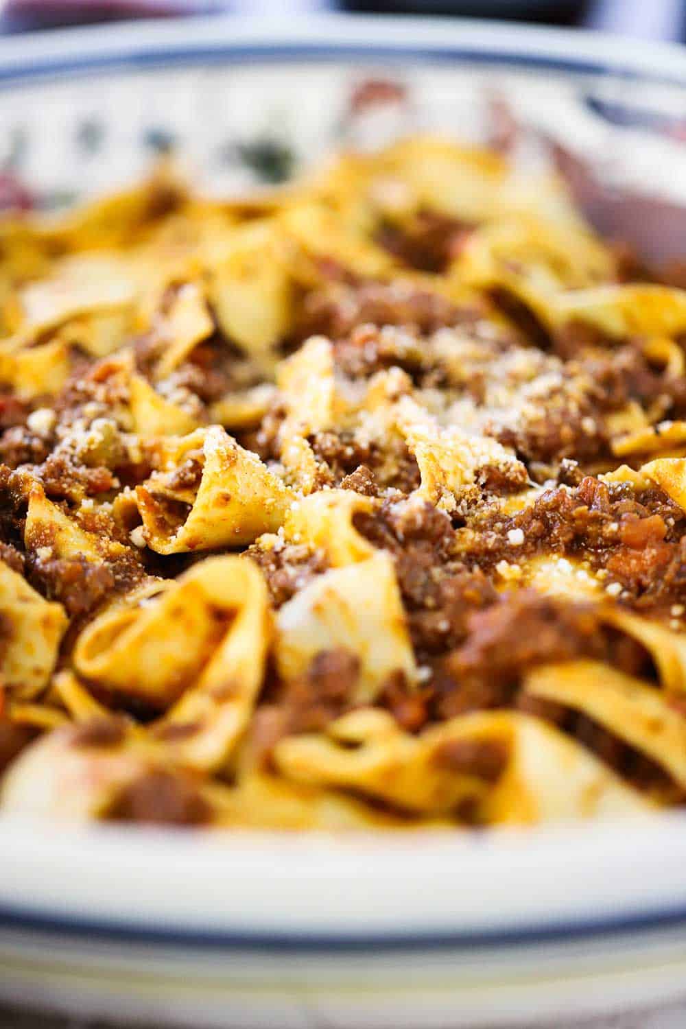 A close-up view of a large Italian pasta bowl filled with homemade pappardelle bolognese. 