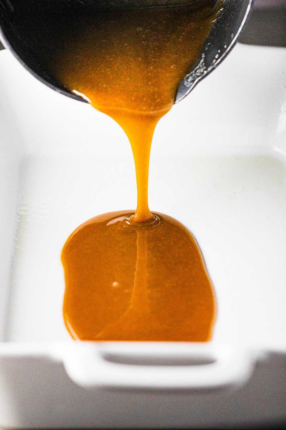 A pan pouring melted caramel sauce into a white baking dish. 