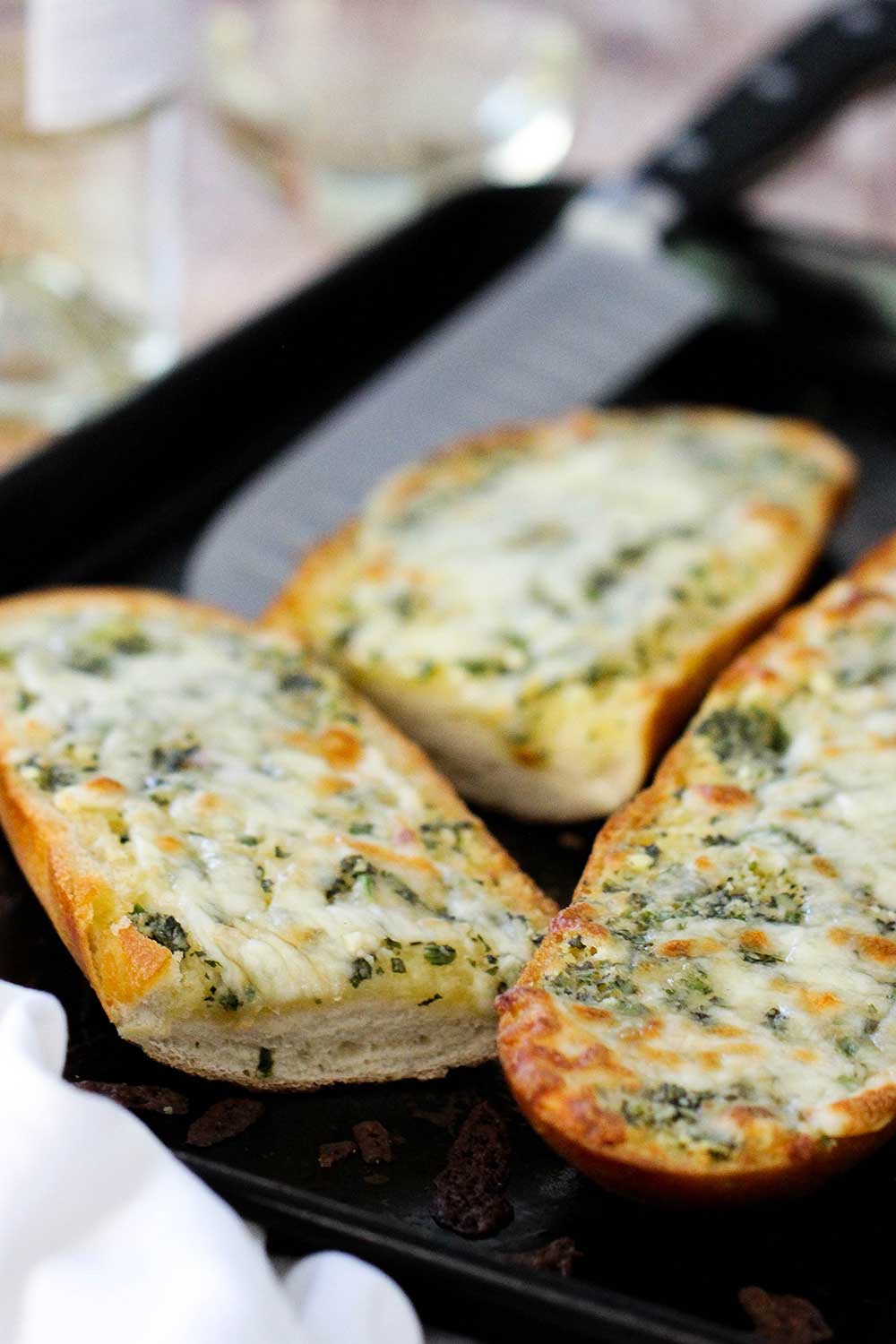 Sliced cheesy garlic bread on baking sheet with a knife nearby. 