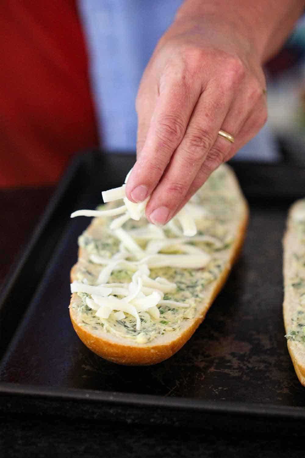 A hand sprinkling mozzarella cheese onto garlic bread. 