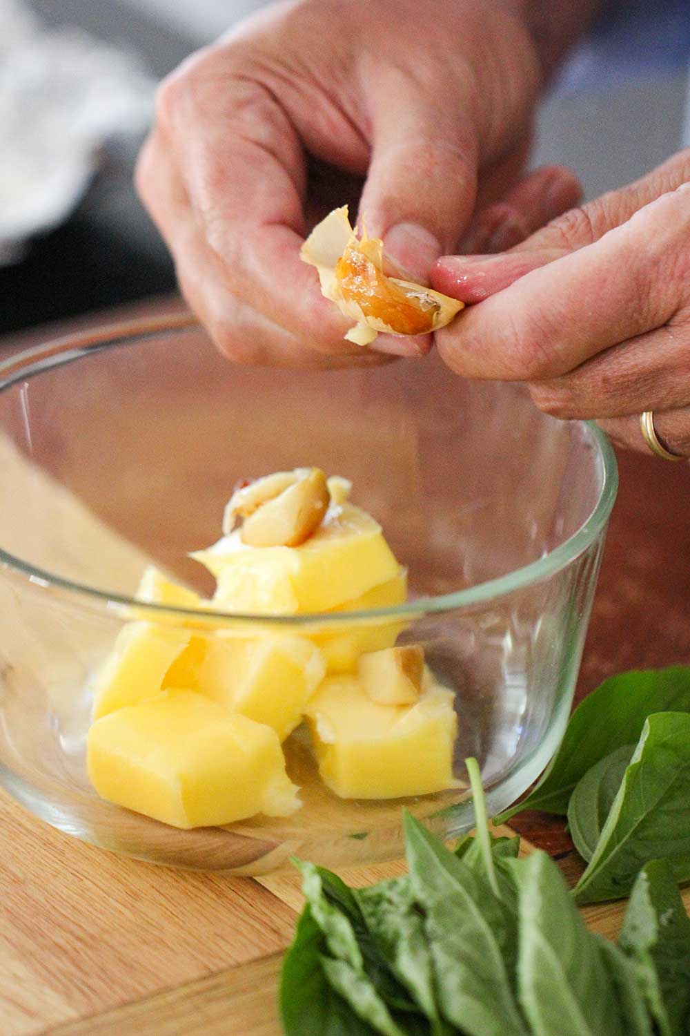 Two hands squeezing roasted garlic into a bowl of softened butter. 