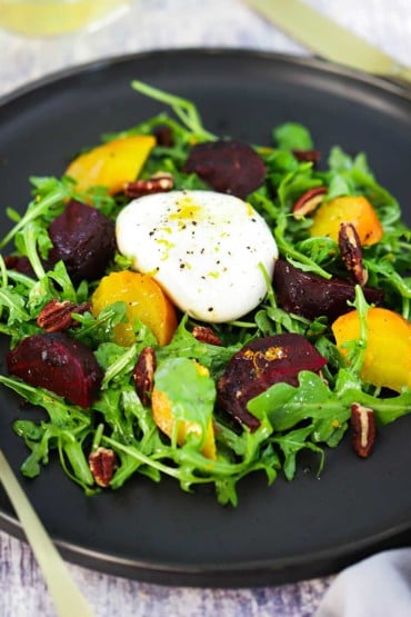A dark circular plate filled with roasted beet and burrata salad.