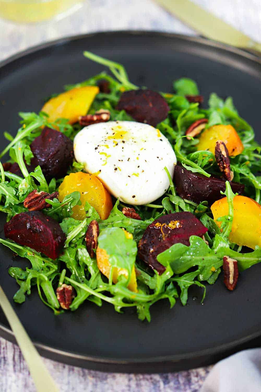 A dark circular plate filled with roasted beet and burrata salad. 