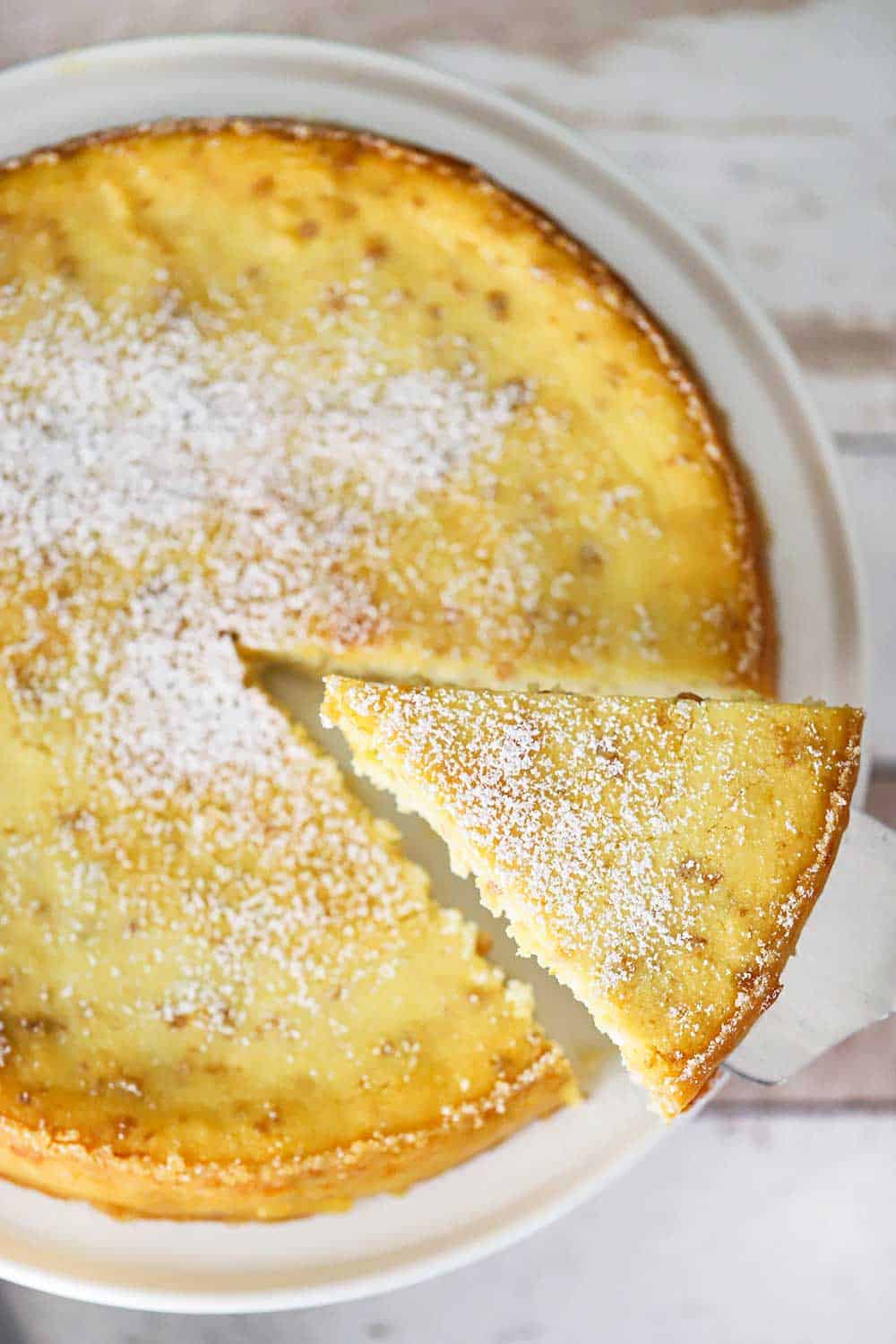 A slice of Italian ricotta cheesecake being lifted out of the cake on a cake stand.