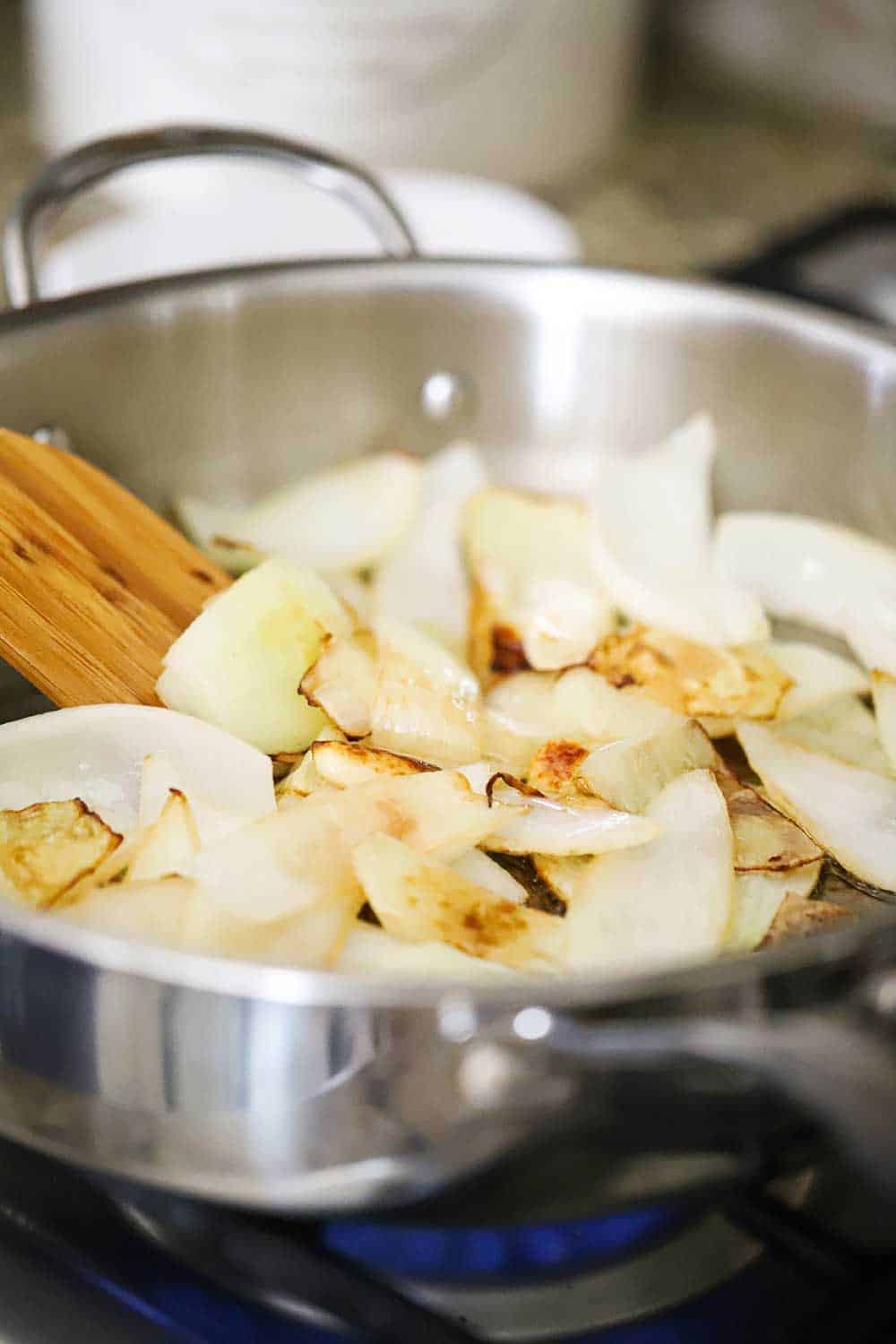 Sliced onions in a large saucepan being roasted and lightly browned. 