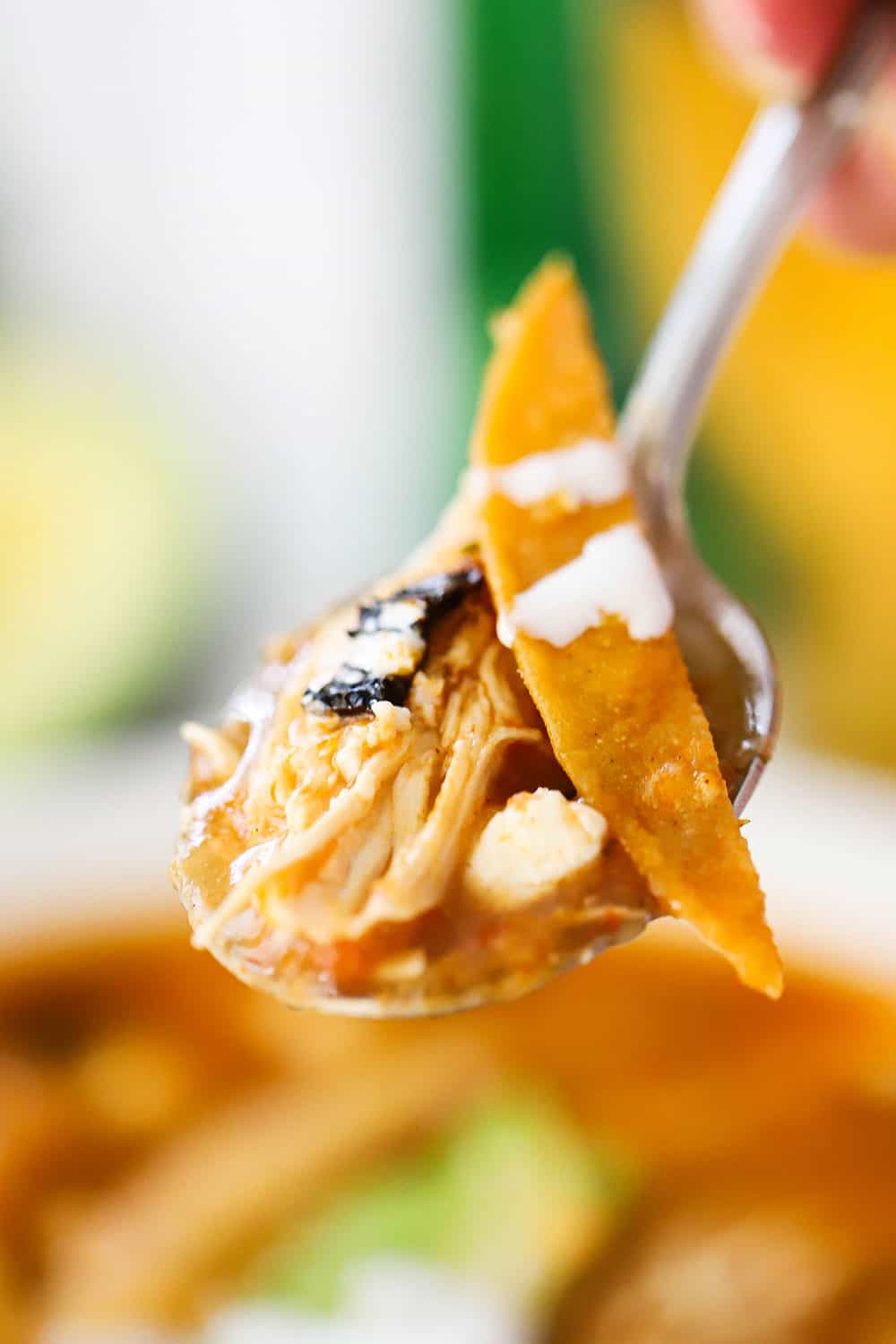 A spoon holding a helping of chicken tortilla soup being held up by a hand. 