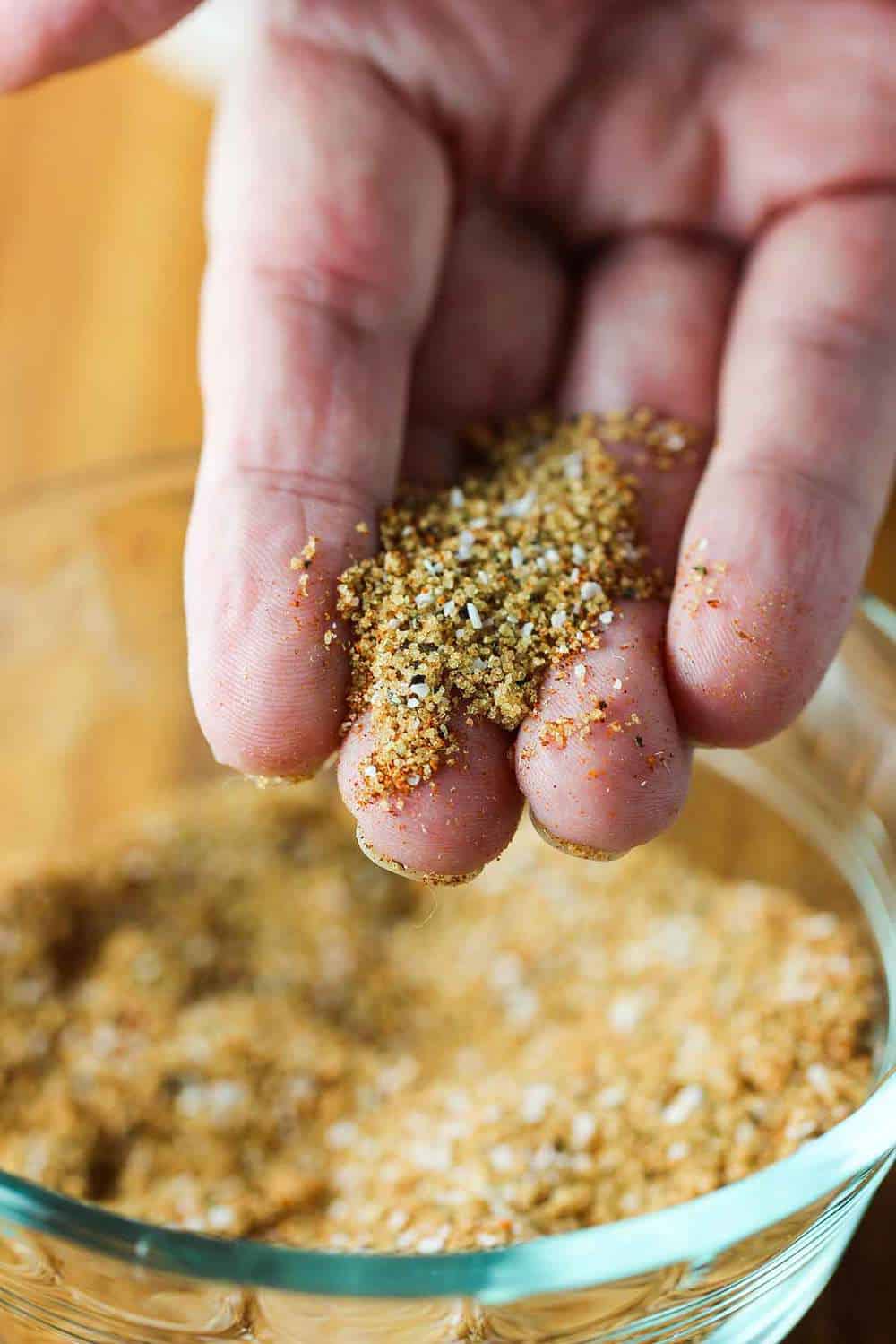 Fingers holding a dry rub for slow cooker baby back ribs.