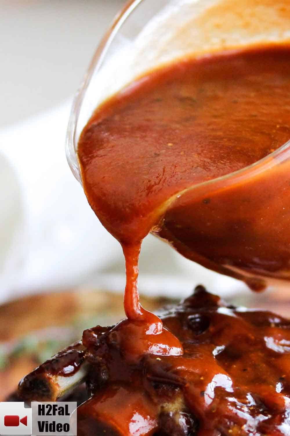 A small glass pitcher pouring easy homemade BBQ sauce over cooked baby back ribs. 