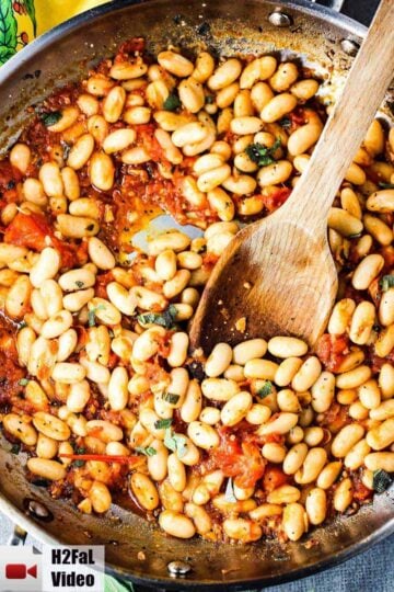 Sautéed white beans with garlic and sage in a large skillet with wooden spoon