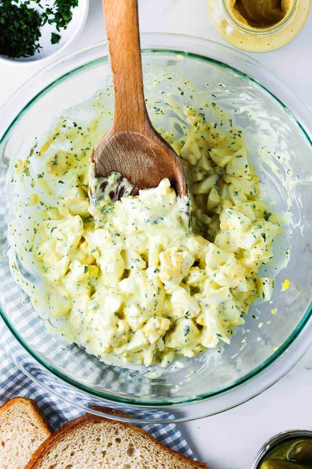 Best-ever egg salad in a glass bowl with a wooden spoon