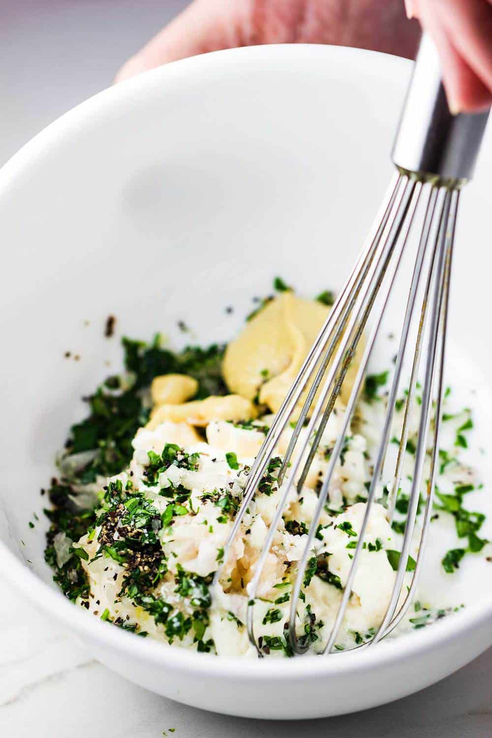 A white bowl filed with egg salad ingredients and a whisk